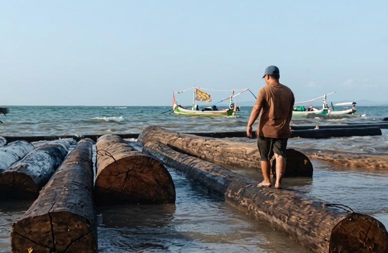 Warga menaiki salah satu kayu gelondongan yang terdampar di pesisir pantai di Sumenep, Jawa Timur. (KOMPAS.COM/ Nur Khalis)